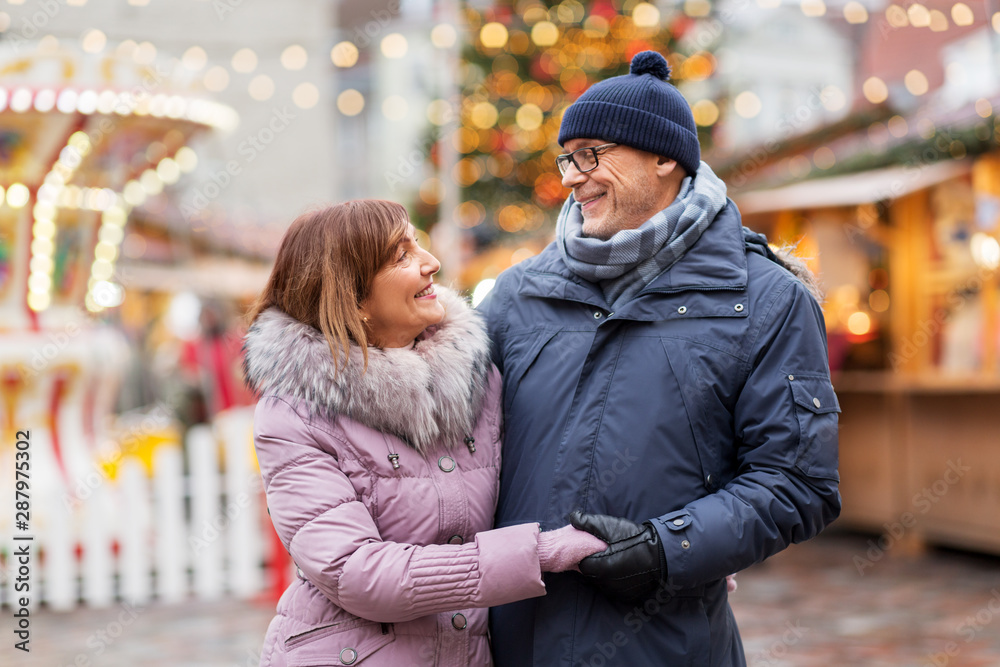 love, winter holidays and people concept - happy senior couple hugging at christmas market on town hall square in tallinn, estonia love, winter holidays and people concept - happy senior couple hugging at christmas market on town hall square in tallinn, estonia