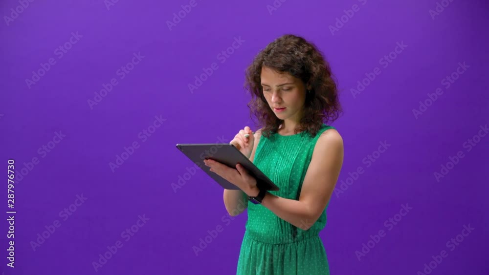 curly girl plays games on an Tablet iPad in a hand on a purple background curly girl plays games on an Tablet iPad in a hand on a purple background