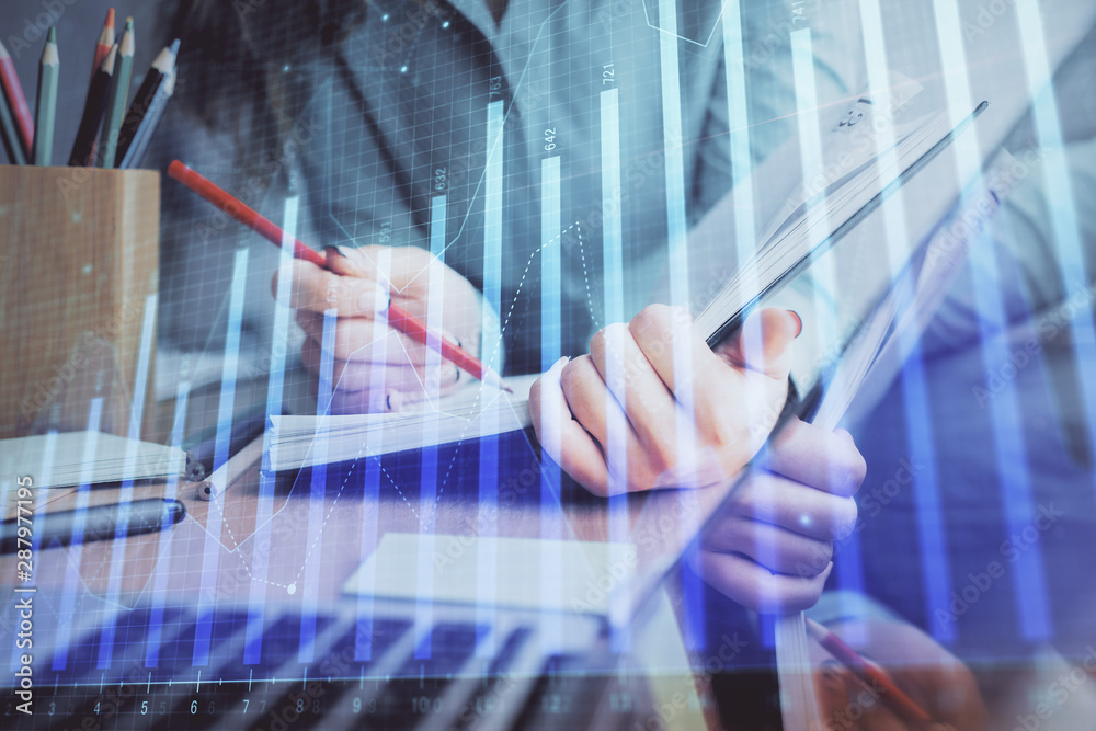 A woman hands writing information about stock market in notepad. Forex chart holograms in front. Concept of research. Multi exposure A woman hands writing information about stock market in notepad. Forex chart holograms in front. Concept of research. Multi exposure