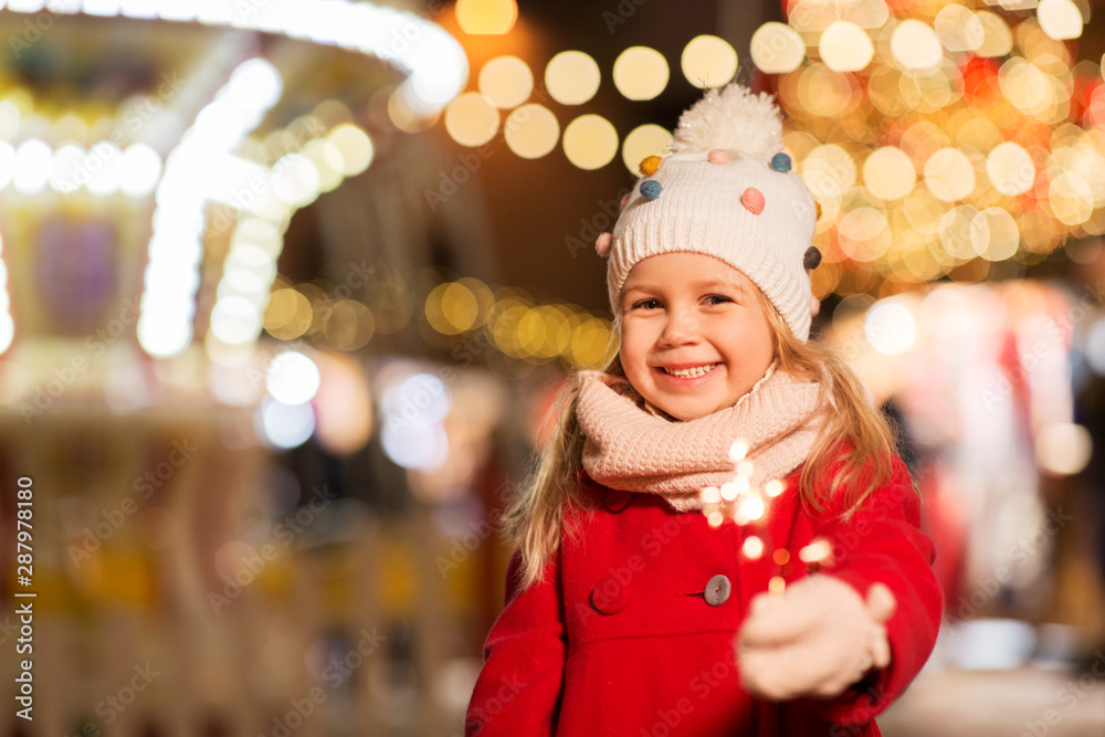 holidays, childhood and people concept - happy little girl with sparkler at christmas market in winter evening