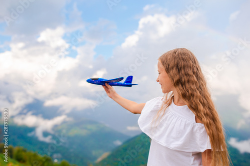Happy little girl with toy airplane in hands in mountains