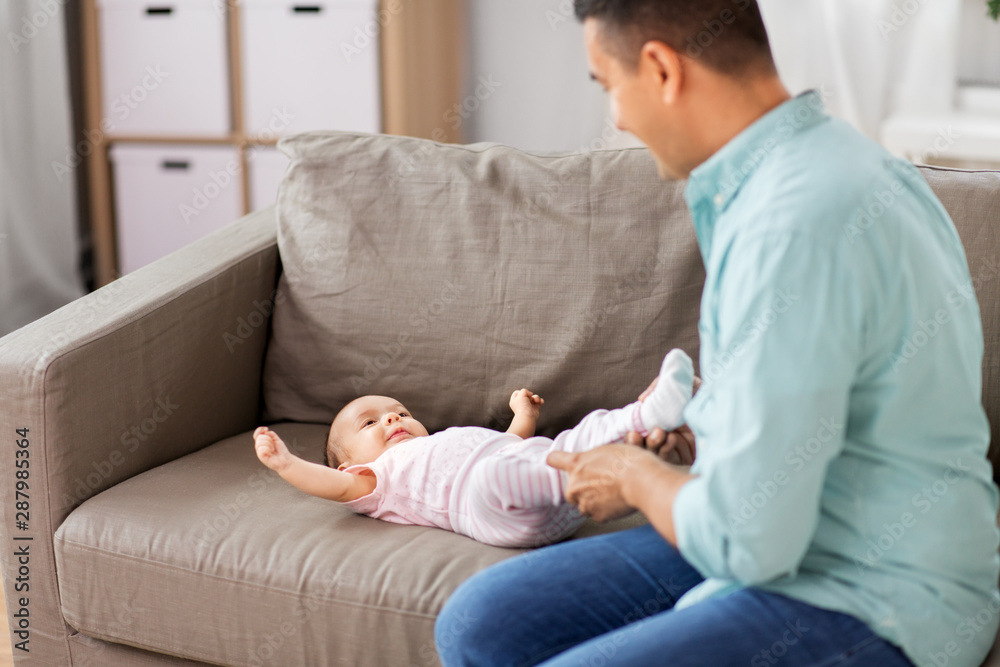 family, parenthood and fatherhood concept - middle aged father playing with little baby daughter lying on sofa at home