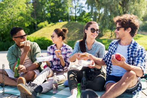 leisure and people concept - group of happy friends having picnic and eating sandwiches at summer park