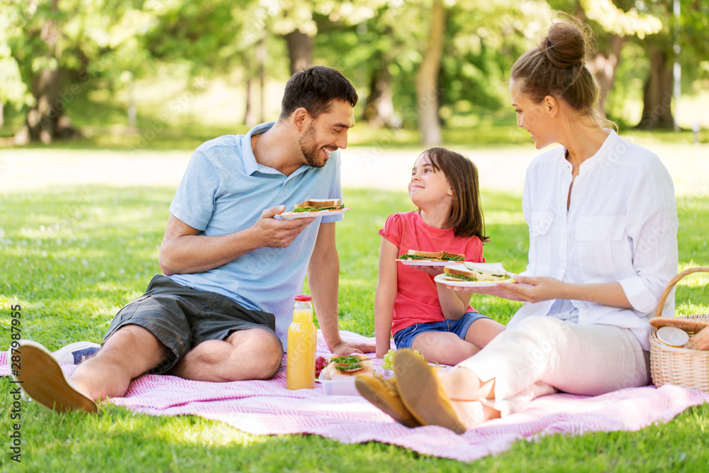 family, leisure and people concept - happy mother, father and daughter having picnic at summer park family, leisure and people concept - happy mother, father and daughter having picnic at summer park
