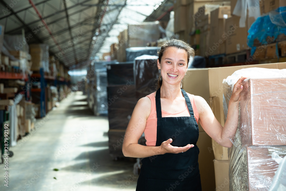 Fototapeta premium Female in apron standing near shelves with cardboard boxes for packaging
