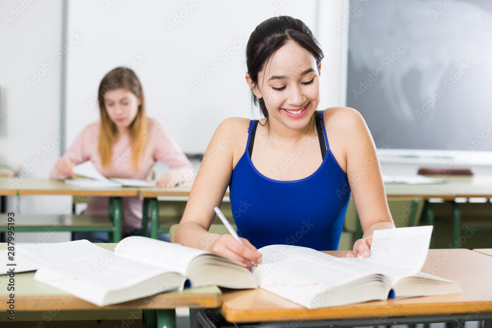 Fototapeta premium Smiling schoolgirl is learning at the desk