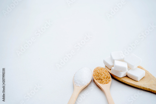 White sugar, brown sugar, sugar cubes, placed in a wooden spoon.