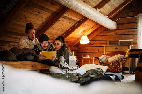 Male and female friends watching movie over digital tablet while relaxing in cottage photo