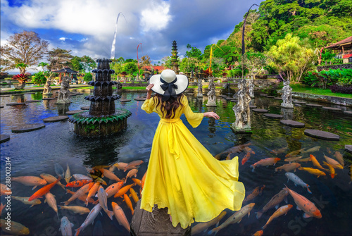 Woman wearing yellow dresses to feed koi fish in Taman Tirtagangga temple on Bali,Indonesia... photo