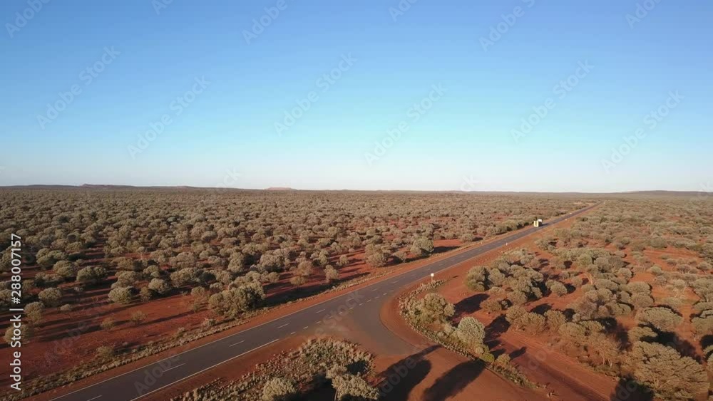 Aerial drone view of flight above highway in outback Australia, with cars and trucks traveling, panorama desert landscape, blue sky and horizon as background. Aerial drone view of flight above highway in outback Australia, with cars and trucks traveling, panorama desert landscape, blue sky and horizon as background.