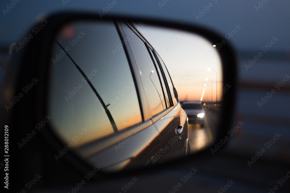 side mirror of a car in which a road with a traveling car is reflected at sunset side mirror of a car in which a road with a traveling car is reflected at sunset