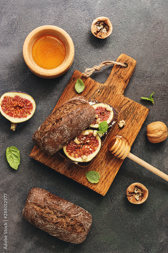 Sandwich with figs, cream cheese, honey and mint leaves on a cutting board, dark rustic background. Top view, flat lay.