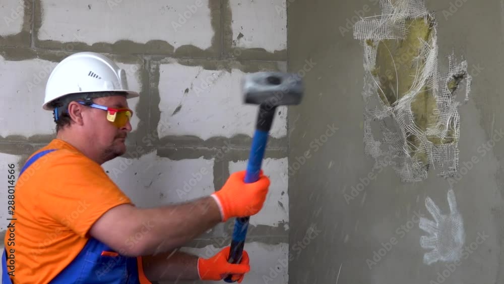 Worker with a sledgehammer breaks a wall, the wall collapses Worker with a sledgehammer breaks a wall, the wall collapses