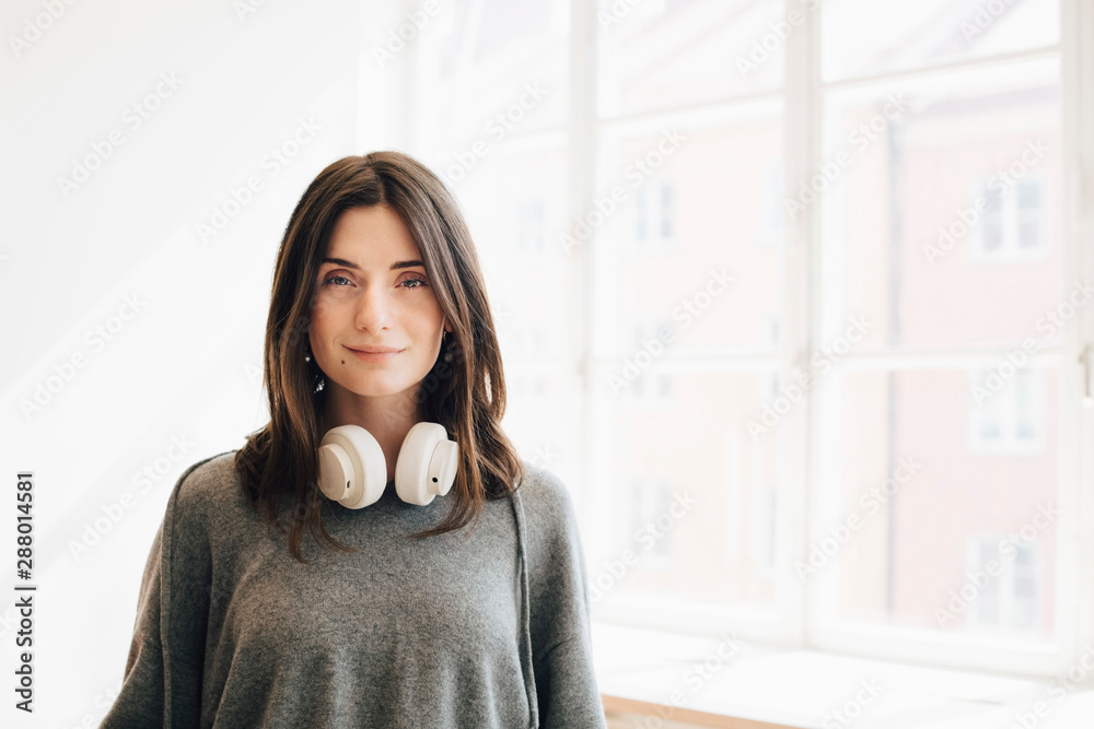 Portrait of female computer programmer with headphone standing against window in office Portrait of female computer programmer with headphone standing against window in office