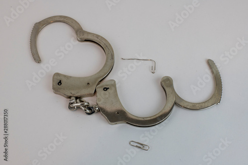 Handcuffs opened with paper clip against white background to illustrate freedom