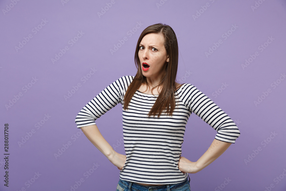Strict irritated young brunette woman in casual striped clothes posing isolated on violet purple background. People lifestyle concept. Mock up copy space. Standing with arms akimbo on waist, swearing. Strict irritated young brunette woman in casual striped clothes posing isolated on violet purple background. People lifestyle concept. Mock up copy space. Standing with arms akimbo on waist, swearing.