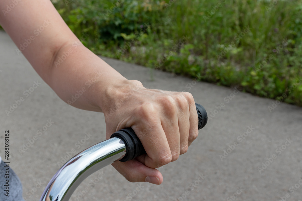 Female hand holding a bicycle handlebar and riding a bike on a road with green grass on roadside, bicycle travelling and journey
