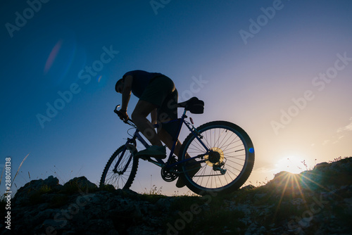 Silhouette of a mountain biker riding his mountain sportbike on top of a cliff ( hill).