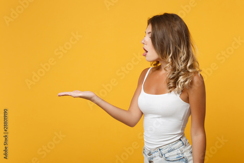 Amazed young woman girl in light casual clothes posing isolated on yellow orange wall background studio portrait. People sincere emotions lifestyle concept. Mock up copy space. Pointing hand aside.