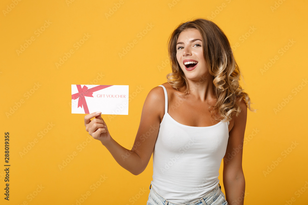 Laughing young woman girl in light casual clothes posing isolated on yellow orange background, studio portrait. People sincere emotions lifestyle concept. Mock up copy space. Holding gift certificate. Laughing young woman girl in light casual clothes posing isolated on yellow orange background, studio portrait. People sincere emotions lifestyle concept. Mock up copy space. Holding gift certificate.