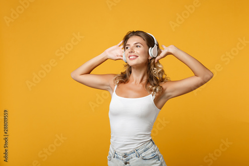 Pretty young woman girl in light casual clothes with headphones posing isolated on yellow orange background, studio portrait. People lifestyle concept. Mock up copy space. Listening music, dancing.