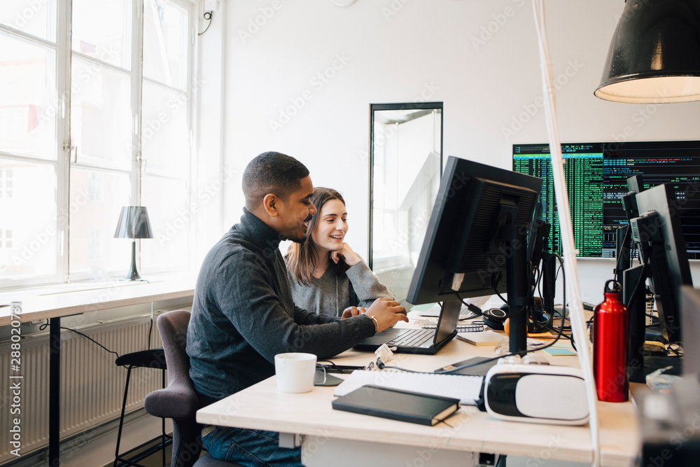 Smiling software programmers discussing over laptop on desk in office Smiling software programmers discussing over laptop on desk in office
