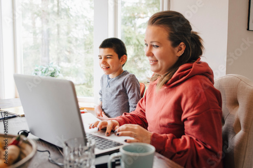 Wallpaper Mural Mother using laptop on table while sitting with autistic son at home Torontodigital.ca