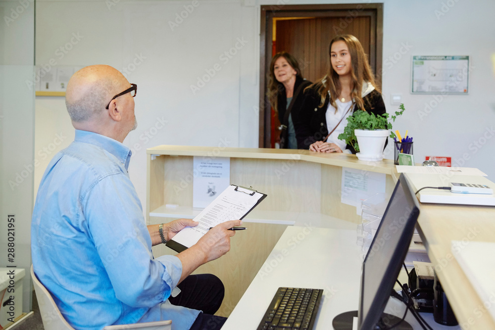 Male therapist with clipboard talking to patient at waiting room Male therapist with clipboard talking to patient at waiting room