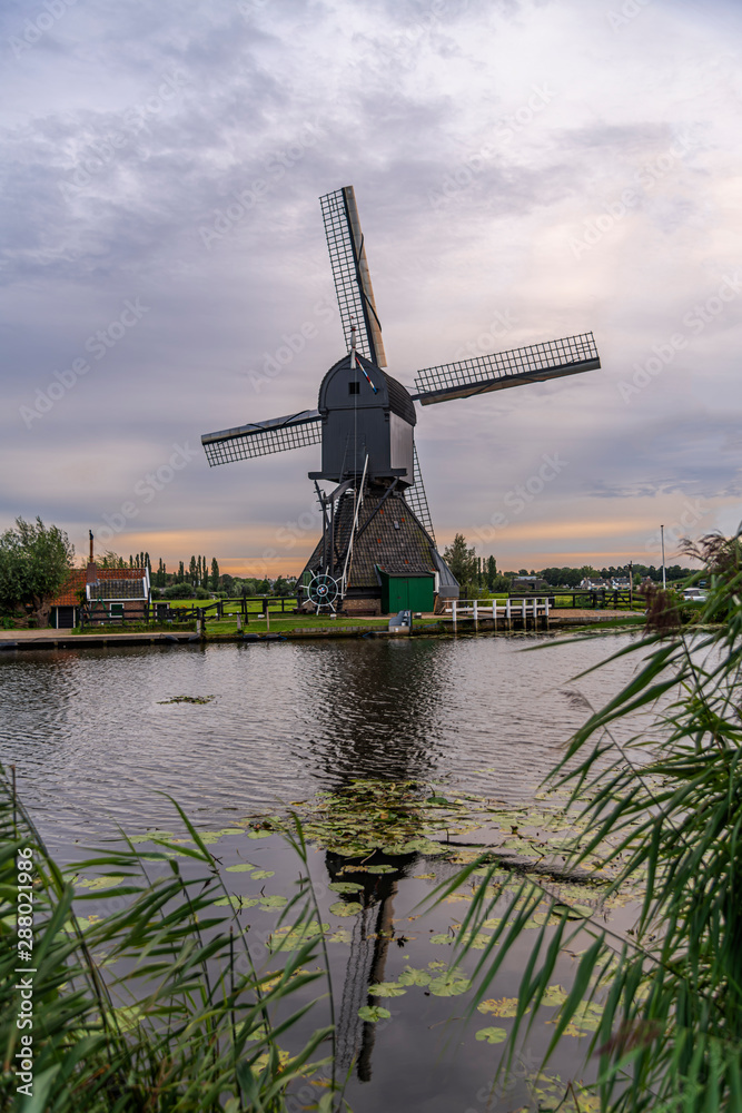 Majestic windmill reflected on the calm canal water during the bleu hour sunset in Alblasserdam city, Netherlands