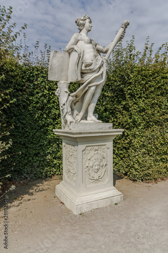 Принти на полотні White marble young woman statue in the garden among trimmed green bushes