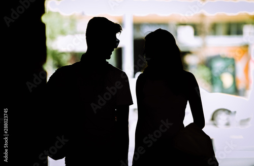 Silhouette of couple with shopping bags holding hands while walking on street