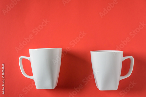 Two white coffee mugs on red background - isolated with copy space above.