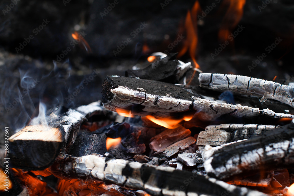 Burned Wood with flames still burning, dark Stone Background of camp fire or Grill Burned Wood with flames still burning, dark Stone Background of camp fire or Grill