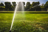 automatic sprinkler system watering the lawn on a background of green grass. Garden irrigation system watering lawn on a sunny summer day. Savings of water from irrigation system with adjustable  head