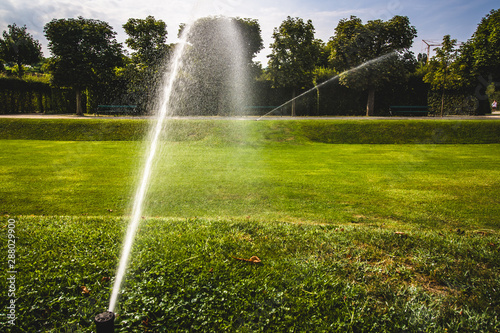 automatic sprinkler system watering the lawn on a background of green grass. Garden irrigation system watering lawn on a sunny summer day. Savings of water from irrigation system with adjustable head