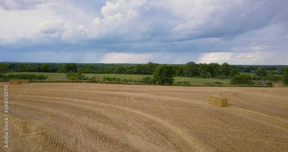 Aerial over a freshly mowed hay field with rain clouds in the distance Aerial over a freshly mowed hay field with rain clouds in the distance