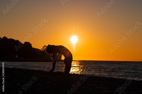Flexible woman practicing yoga activity on the beach during the sunset in camel pose, relaxation, wellbeing, Zen attitude, good posture reflections in the water