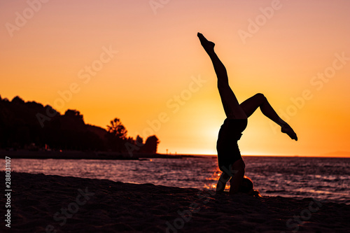 Flexible woman practicing vinyasa yoga and gymnastics on the beach at sunset, wellbeing, good posture, zen attitude, healthy, pacific ocean view, relaxation