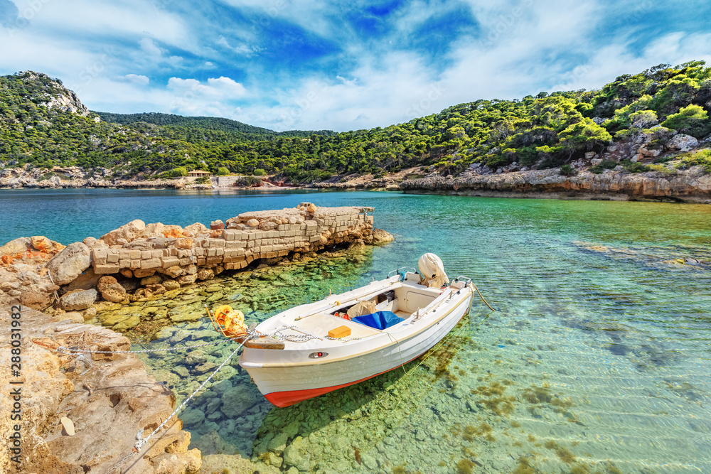 Greece, old wooden fishing boat in lagoon anchored in picturesque lagoon with turquoise waters at the green coastal forest and blue sky background. Greek islands concept. Mediterranean background.