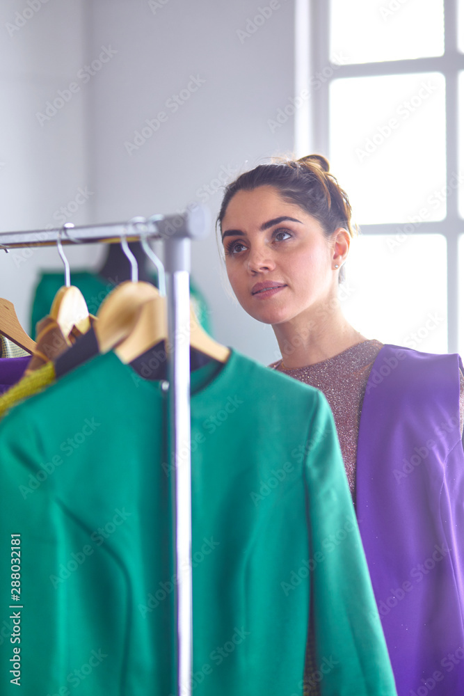 Beautiful young stylist holding clipboard near rack with design Beautiful young stylist holding clipboard near rack with design
