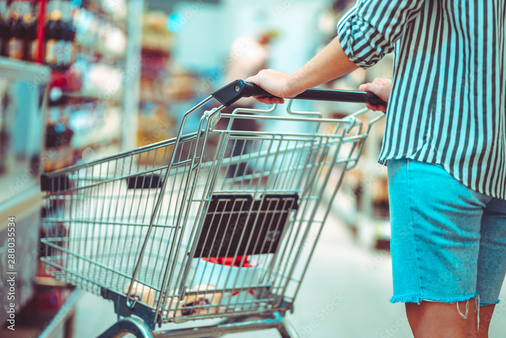 Shopper with shopping cart in supermarket aisle. Buying food in grocery store. Grocery shopping