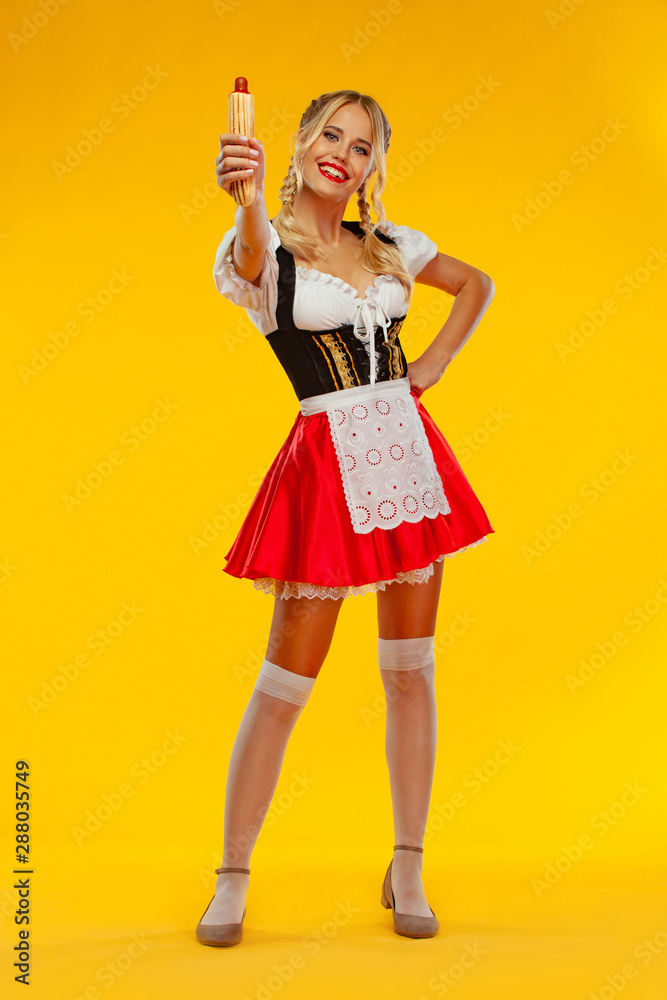 Young sexy Oktoberfest girl waitress, wearing a traditional Bavarian or  german dirndl with french hot dogs isolated on yellow background. Full  height photo. Photos | Adobe Stock