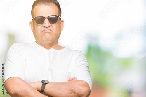 Middle age arab man wearig white t-shirt and sunglasses over isolated background skeptic and nervous, disapproving expression on face with crossed arms. Negative person. photo