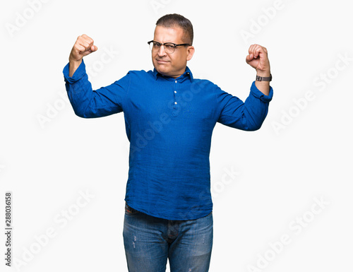 Middle age arab man wearing glasses over isolated background showing arms muscles smiling proud. Fitness concept.