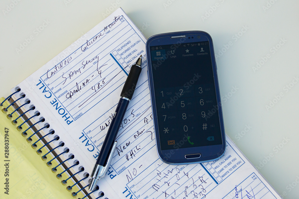 Smartphone, pen, hand, note book or phone book or organizer with some notes, info or phones number on a white table. Plans and agenda. Keyboard on. Smartphone, pen, hand, note book or phone book or organizer with some notes, info or phones number on a white table. Plans and agenda. Keyboard on.