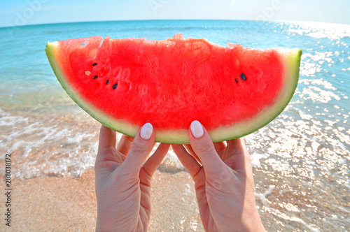 Summertime concept with watermelon slice in woman hand against the sea