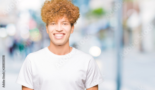 Young handsome man with afro hair wearing casual white t-shirt with a happy and cool smile on face. Lucky person.