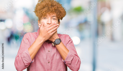 Young handsome business man with afro hair shocked covering mouth with hands for mistake. Secret concept.