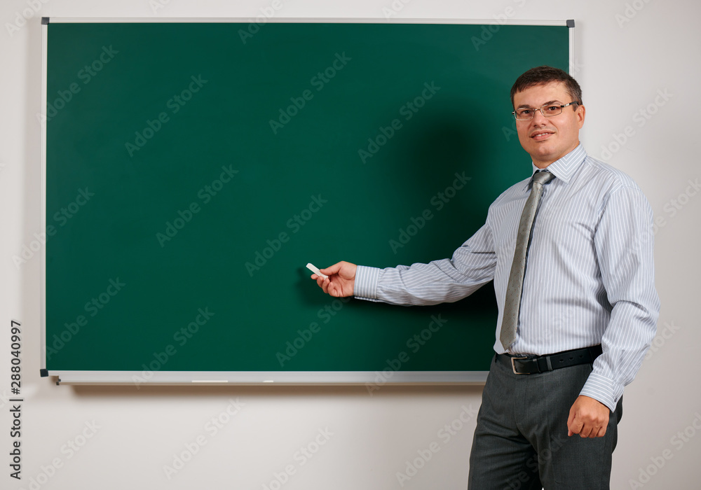 Portrait of a man dressed as a school teacher in business suit, posing at blackboard background - learning and education concept