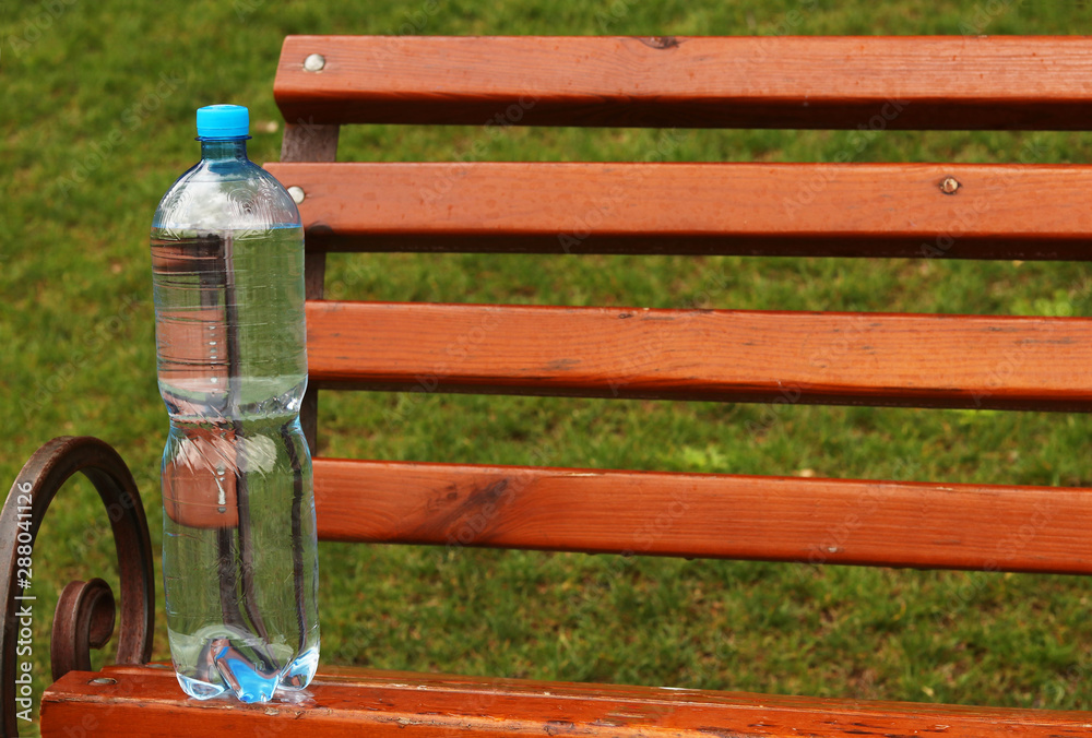 Plastic bottle with mineral water stands on a park bench, horizontal orientation, copy space Plastic bottle with mineral water stands on a park bench, horizontal orientation, copy space